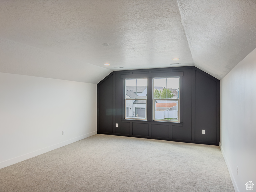 Additional living space featuring light colored carpet, a textured ceiling, and vaulted ceiling