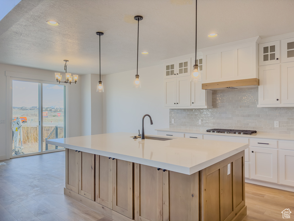 Kitchen featuring decorative light fixtures, backsplash, an island with sink, sink, and light wood-type flooring