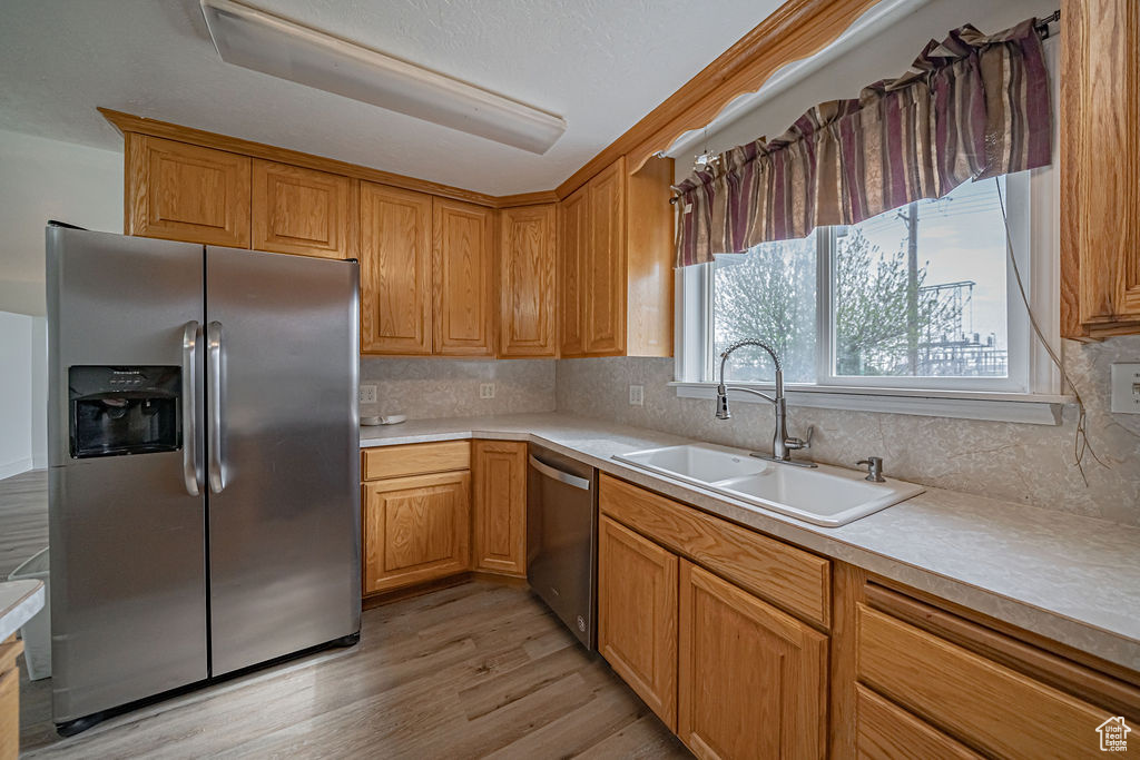 Kitchen with sink, light hardwood / wood-style flooring, tasteful backsplash, and stainless steel appliances