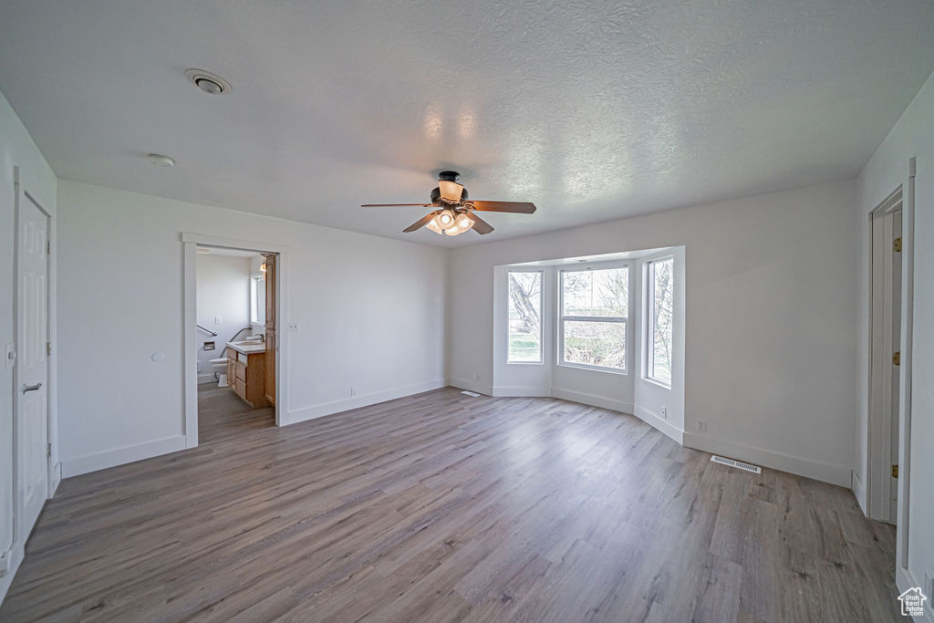 Interior space with hardwood / wood-style floors, connected bathroom, ceiling fan, and a textured ceiling