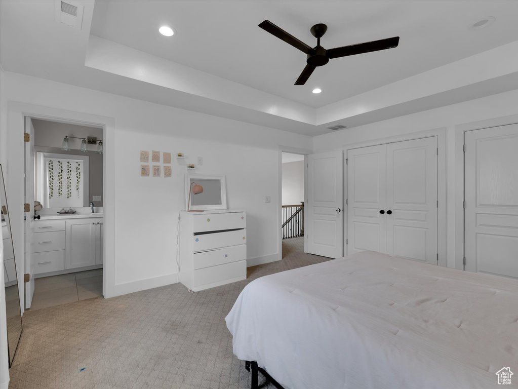 Carpeted bedroom with a closet, ceiling fan, a raised ceiling, and ensuite bath