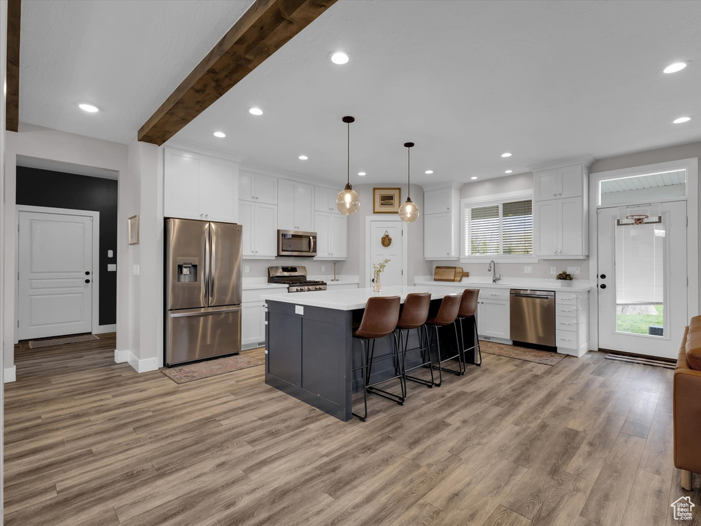 Kitchen featuring light hardwood / wood-style flooring, stainless steel appliances, beam ceiling, a wealth of natural light, and a center island