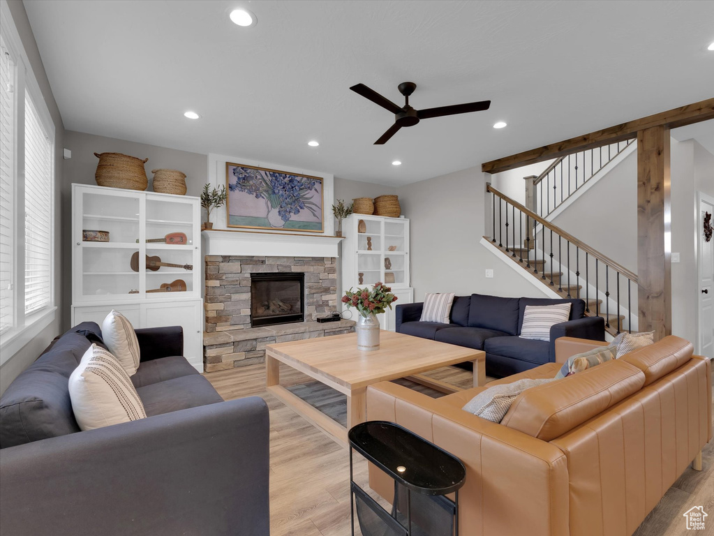 Living room featuring a stone fireplace, ceiling fan, and light wood-type flooring