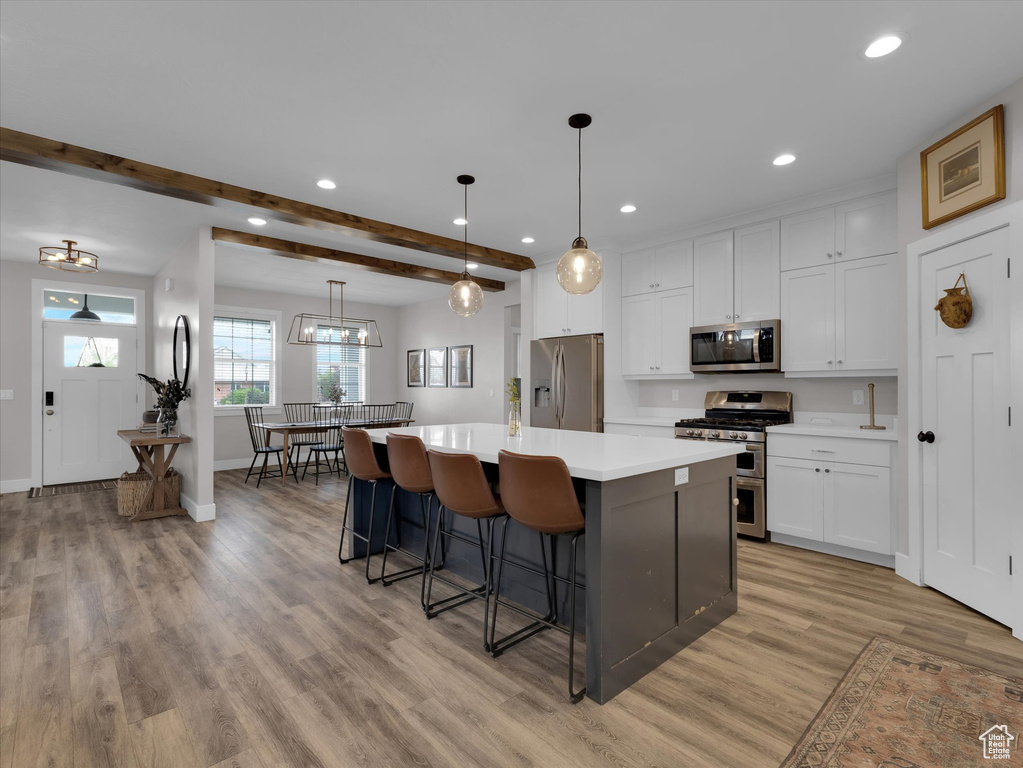 Kitchen with white cabinets, light hardwood / wood-style flooring, appliances with stainless steel finishes, beam ceiling, and a kitchen island