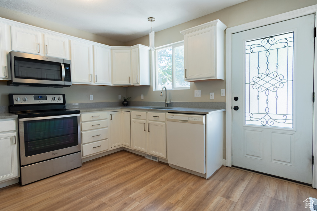 Kitchen featuring appliances with stainless steel finishes, white cabinets, sink, light hardwood / wood-style floors, and pendant lighting