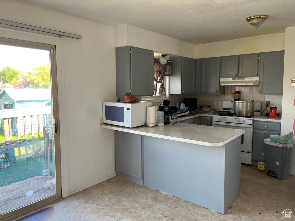Kitchen with gray cabinets, white appliances, tasteful backsplash, and kitchen peninsula