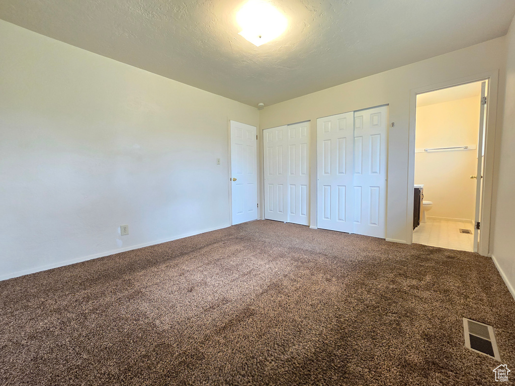 Unfurnished bedroom with multiple closets, connected bathroom, and carpet flooring