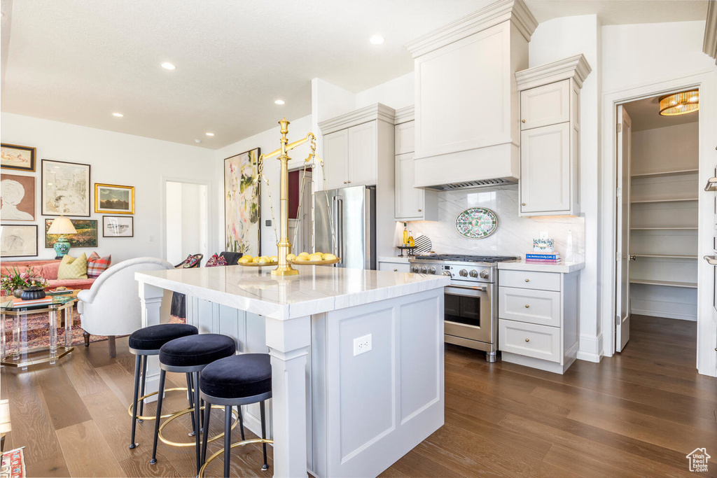 Kitchen featuring premium appliances, a kitchen island, backsplash, white cabinetry, and dark hardwood / wood-style flooring