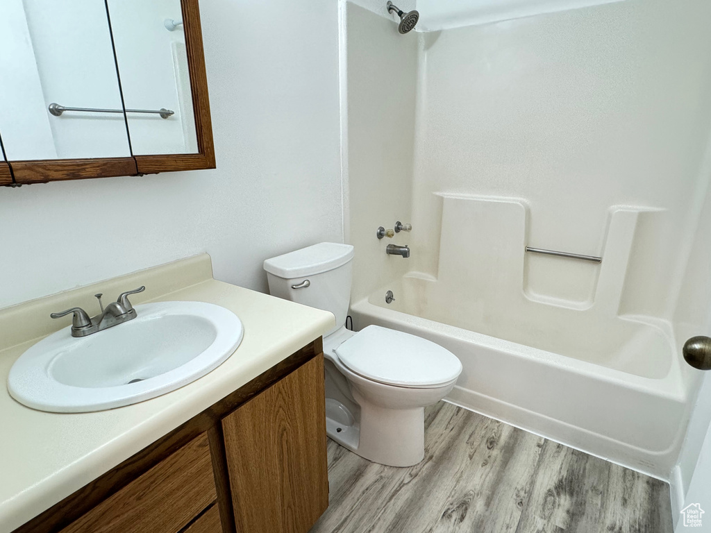 Full bathroom with hardwood / wood-style floors, shower / tub combination, vanity with extensive cabinet space, and toilet