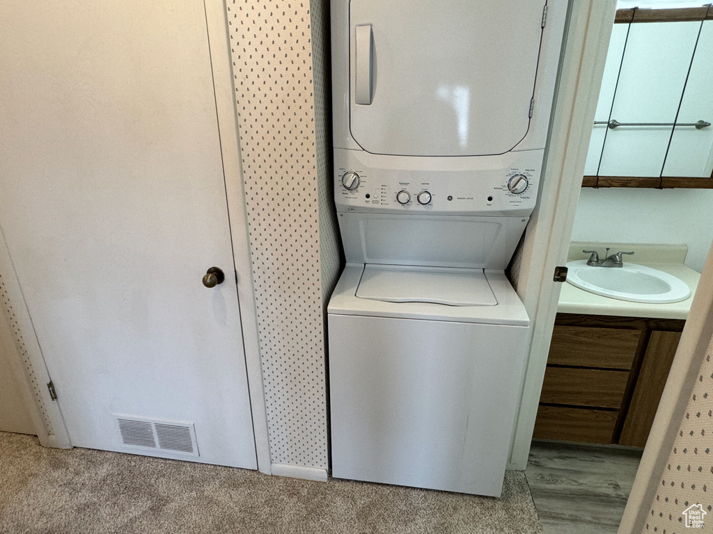 Laundry room with sink, light carpet, and stacked washing maching and dryer