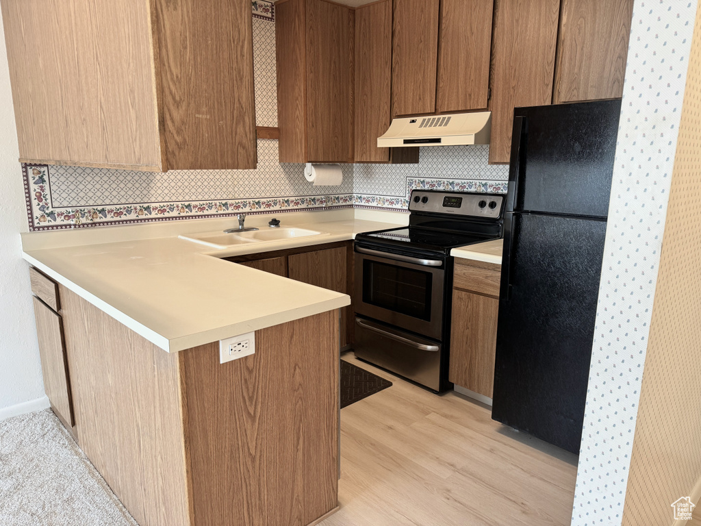 Kitchen with black fridge, electric range, tasteful backsplash, sink, and light wood-type flooring