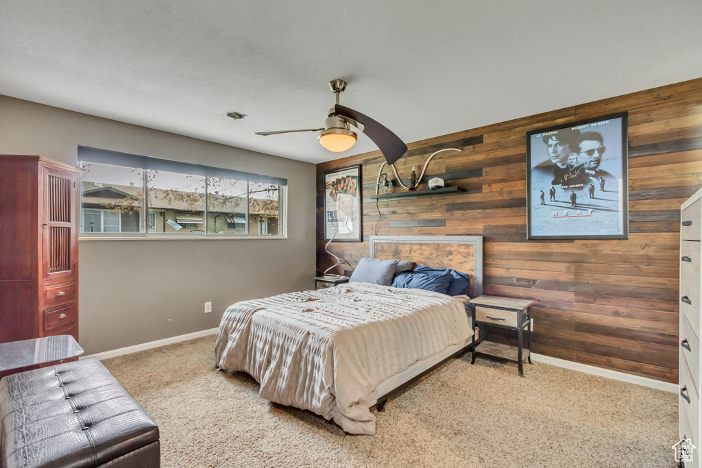 Carpeted bedroom featuring wooden walls and ceiling fan