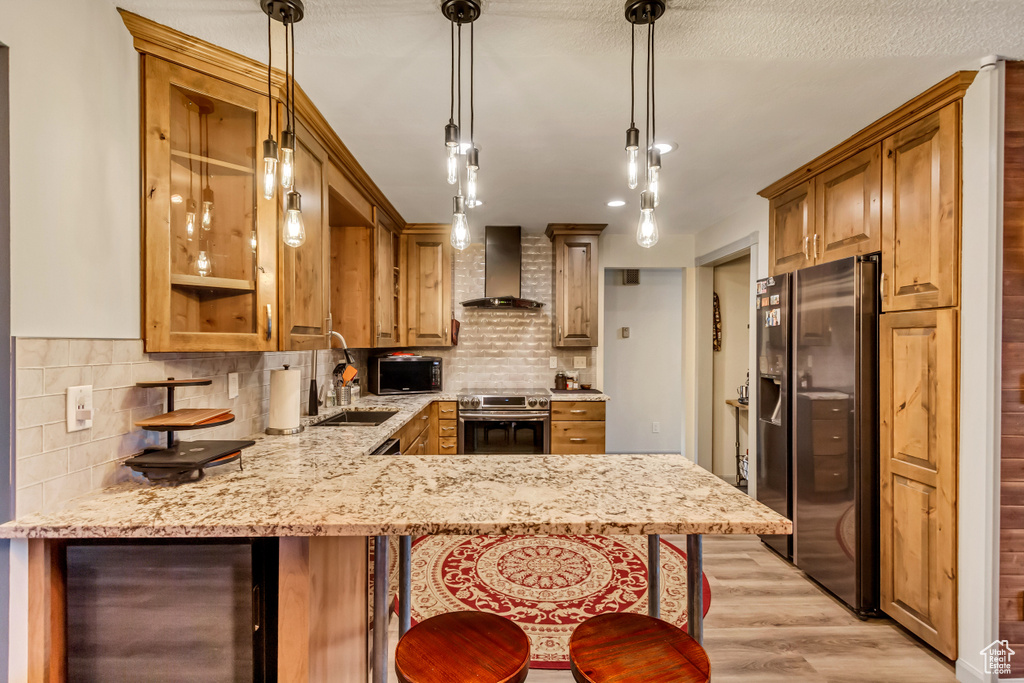 Kitchen featuring light wood-type flooring, wall chimney range hood, stainless steel appliances, sink, and tasteful backsplash