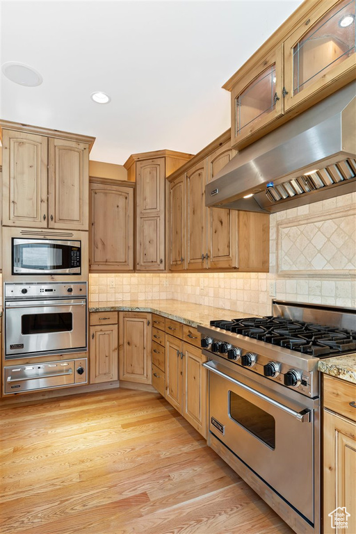 Kitchen with tasteful backsplash, light stone countertops, stainless steel appliances, and light wood-type flooring
