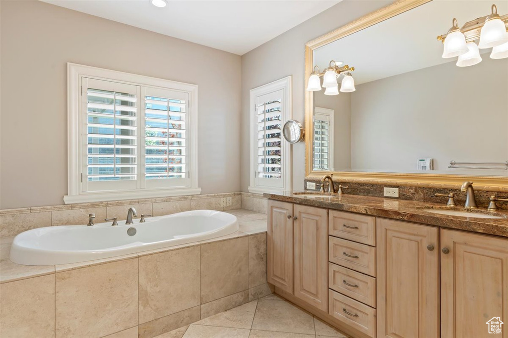 Bathroom featuring tiled bath, oversized vanity, tile floors, and dual sinks