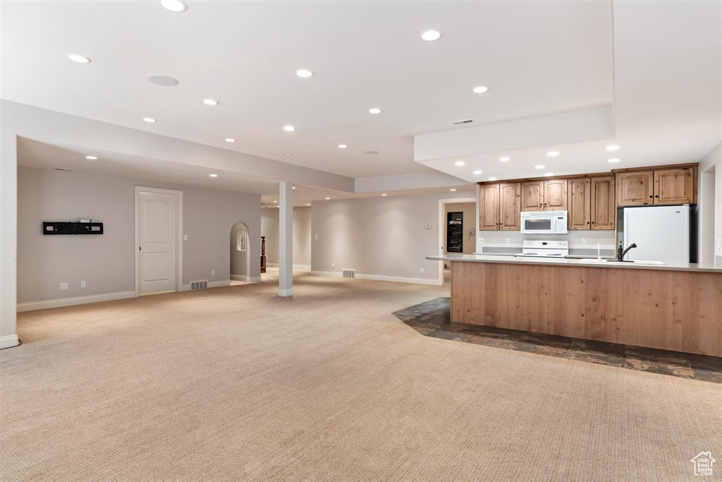 Kitchen featuring light carpet, white appliances, decorative columns, a large island, and a tray ceiling