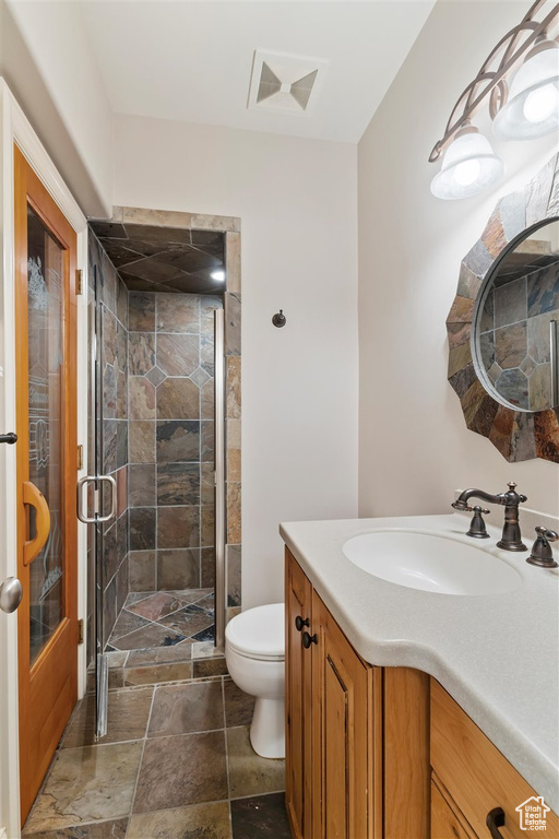 Bathroom with an enclosed shower, toilet, tile flooring, and vanity