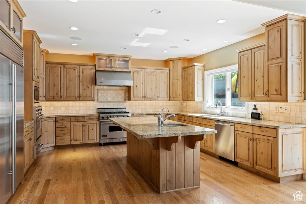 Kitchen featuring a center island with sink, light hardwood / wood-style floors, tasteful backsplash, premium appliances, and sink
