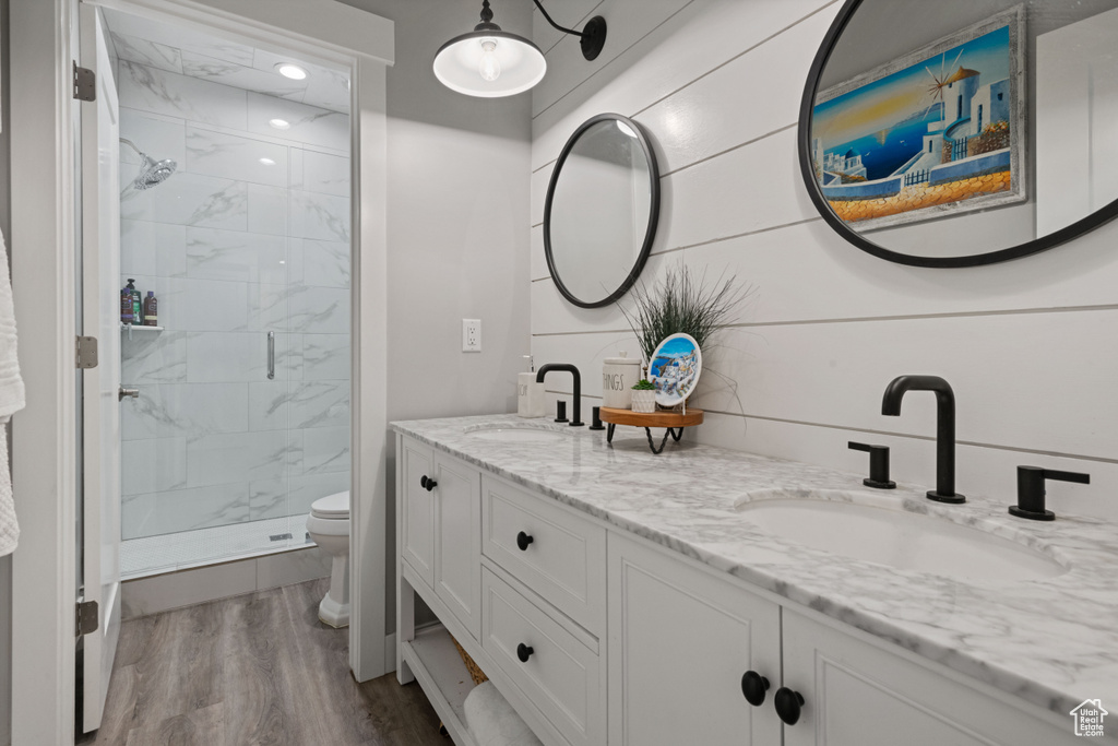 Bathroom featuring tiled shower, toilet, hardwood / wood-style floors, and double sink vanity