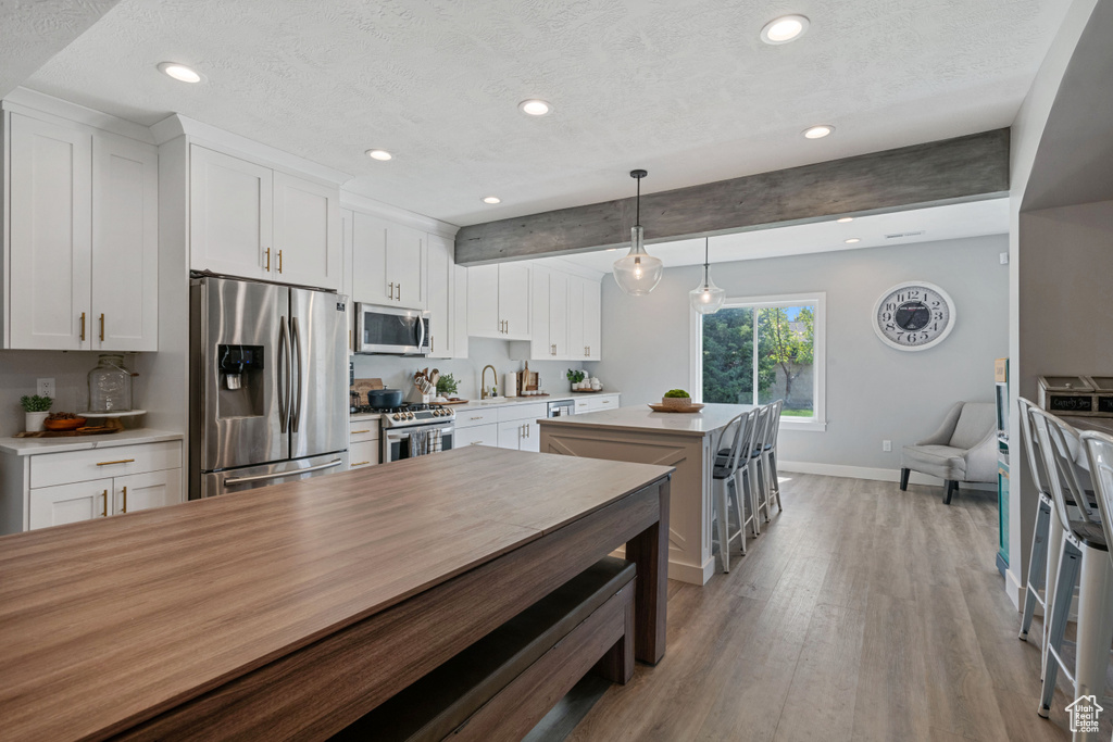 Kitchen featuring hanging light fixtures, white cabinets, stainless steel appliances, light hardwood / wood-style floors, and a textured ceiling
