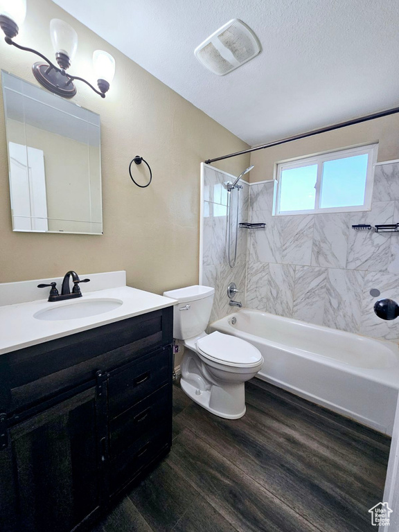 Full bathroom featuring tiled shower / bath combo, oversized vanity, hardwood / wood-style flooring, toilet, and a textured ceiling