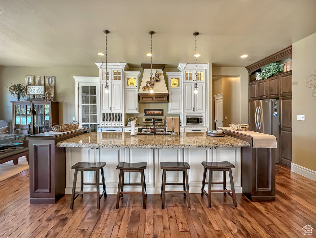 Kitchen with a kitchen bar, a spacious island, stainless steel appliances, hardwood / wood-style flooring, and custom range hood