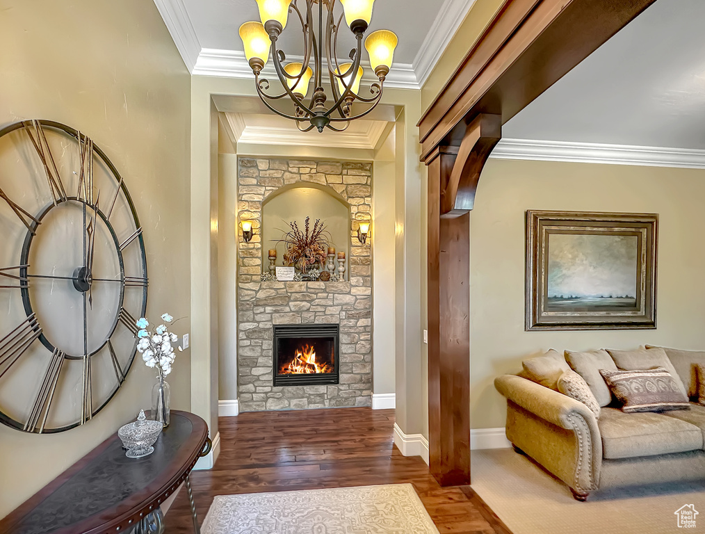 Entrance foyer with a stone fireplace, crown molding, hardwood / wood-style flooring, and an inviting chandelier