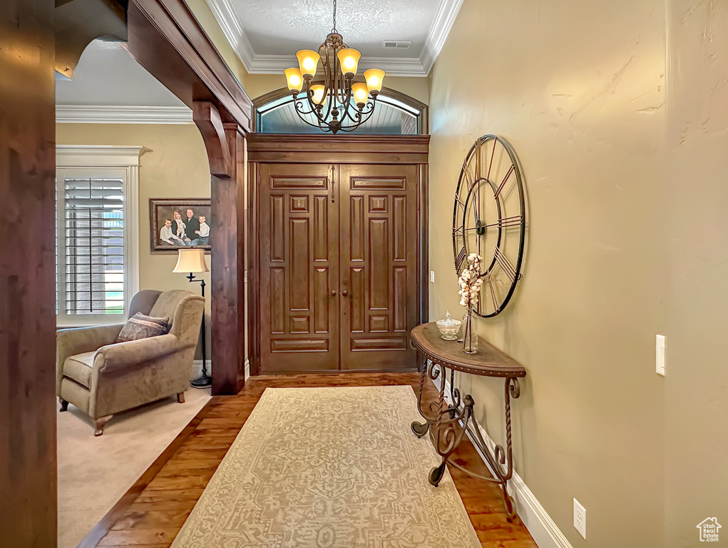 Foyer featuring wood-type flooring, a textured ceiling, a notable chandelier, and ornamental molding