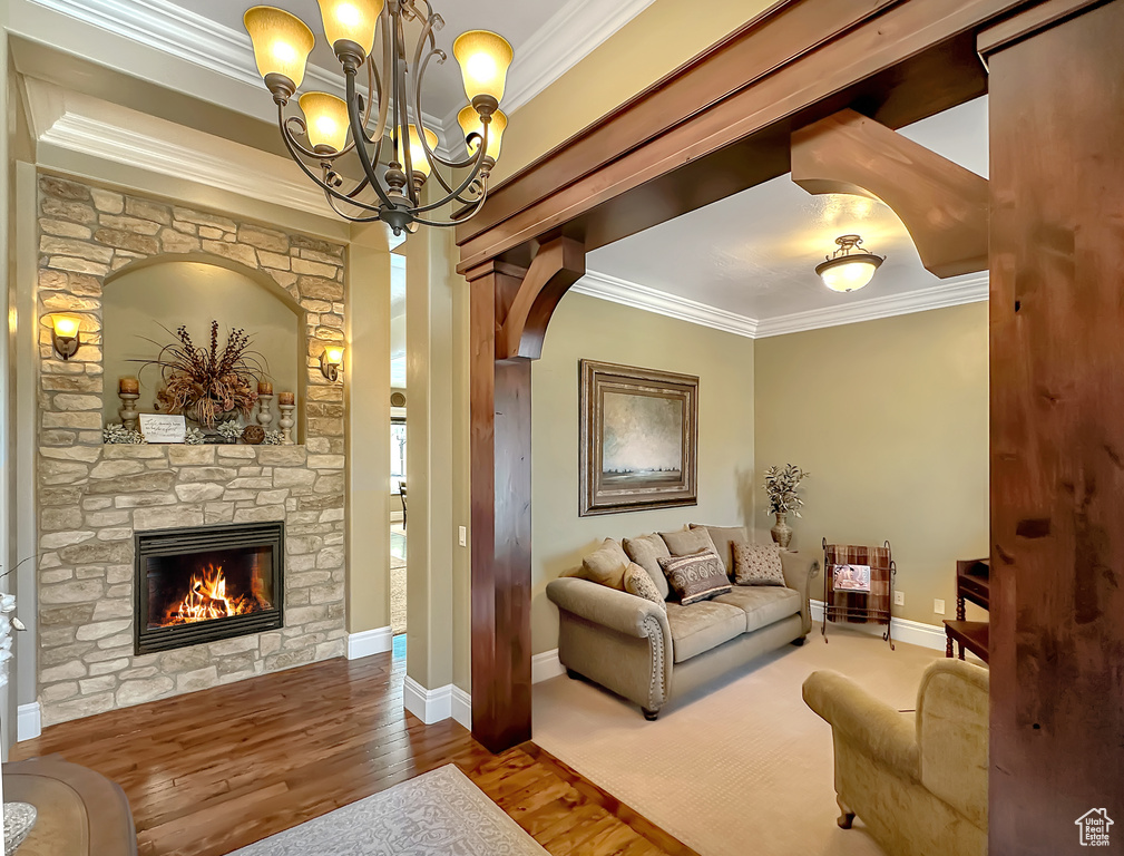 Living room featuring wood-type flooring, a fireplace, a chandelier, and ornamental molding
