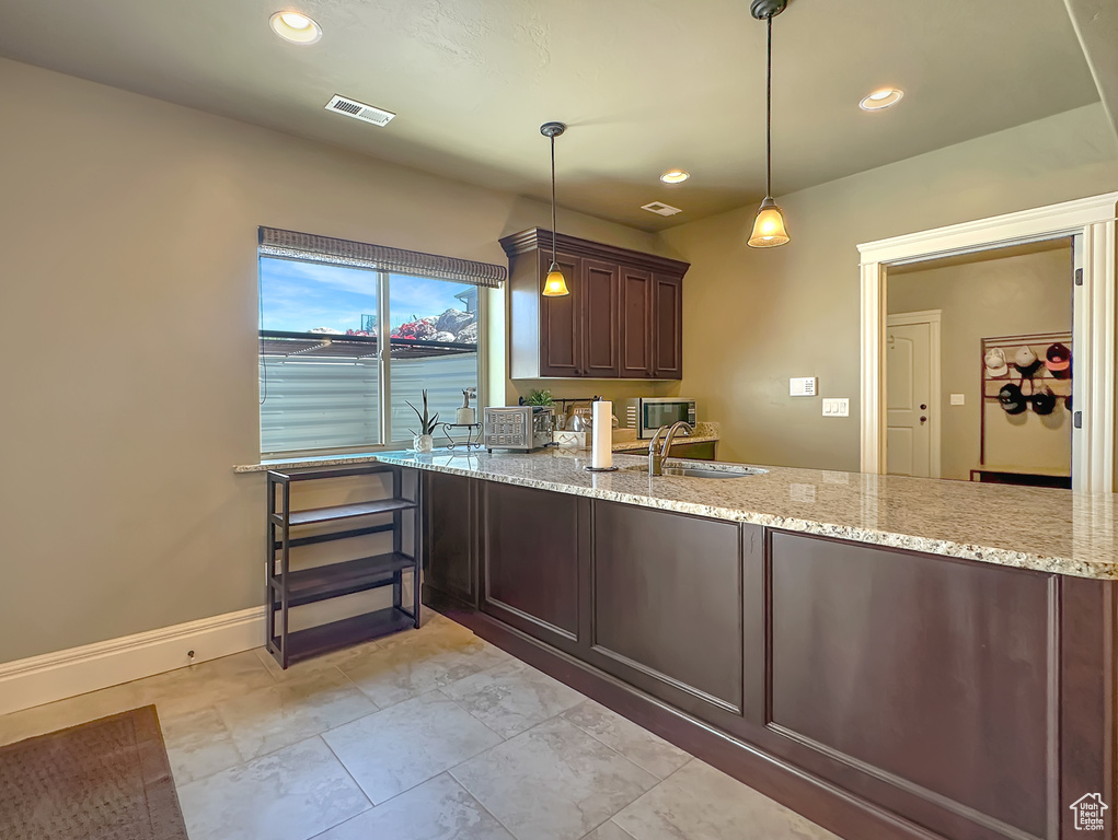 Kitchen featuring dark brown cabinets, light stone countertops, decorative light fixtures, sink, and light tile floors