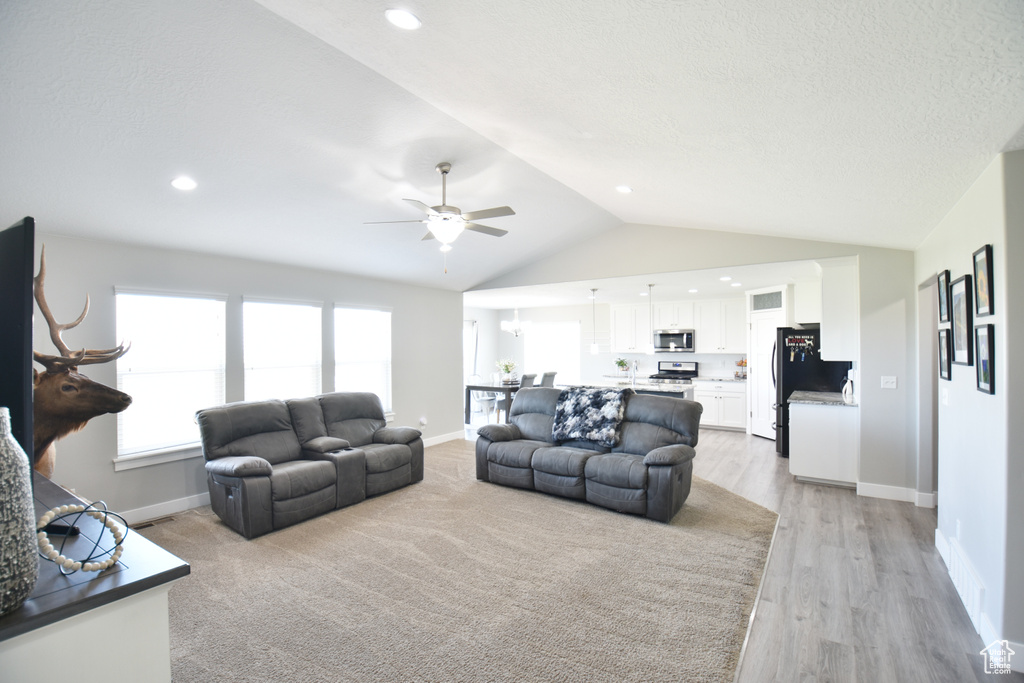 Living room featuring lofted ceiling, ceiling fan, and light carpet