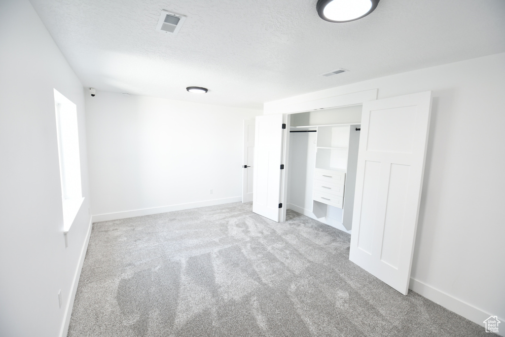 Unfurnished bedroom featuring light colored carpet, a textured ceiling, and a closet