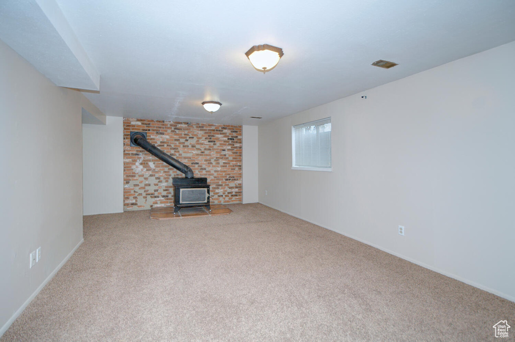 Unfurnished living room featuring a wood stove, carpet, and brick wall