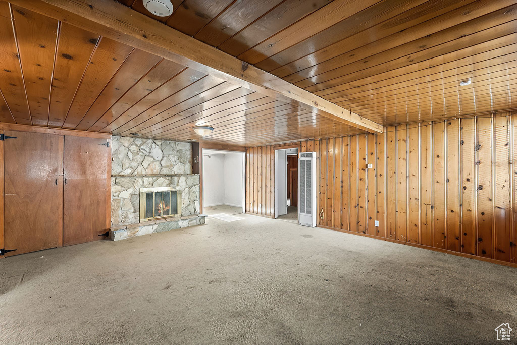 Unfurnished living room with wooden ceiling, wood walls, carpet flooring, and a stone fireplace