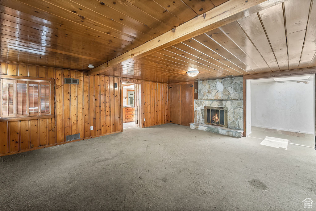 Unfurnished living room featuring wooden ceiling, wooden walls, a stone fireplace, and carpet flooring