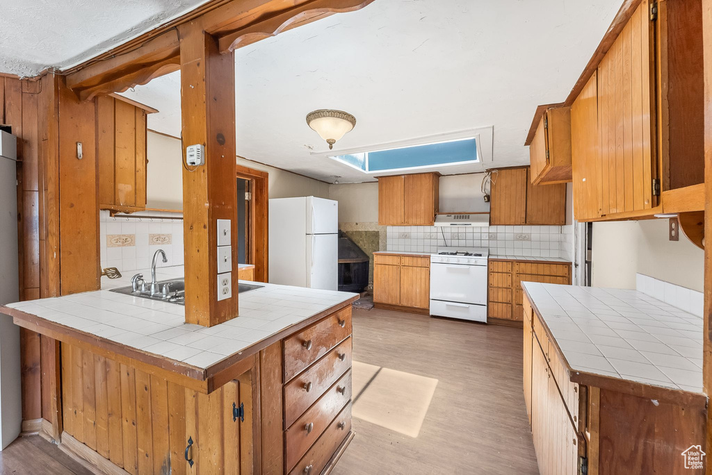 Kitchen featuring tile counters, white appliances, tasteful backsplash, and light wood-type flooring