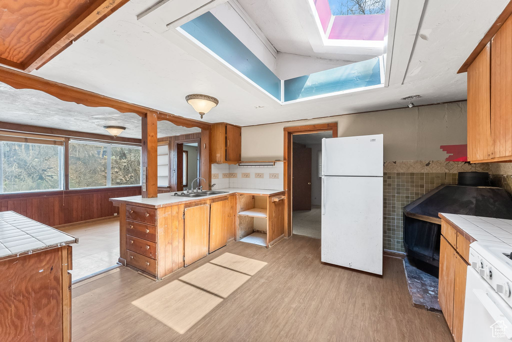 Kitchen with white fridge, light hardwood / wood-style flooring, lofted ceiling with skylight, tile countertops, and sink