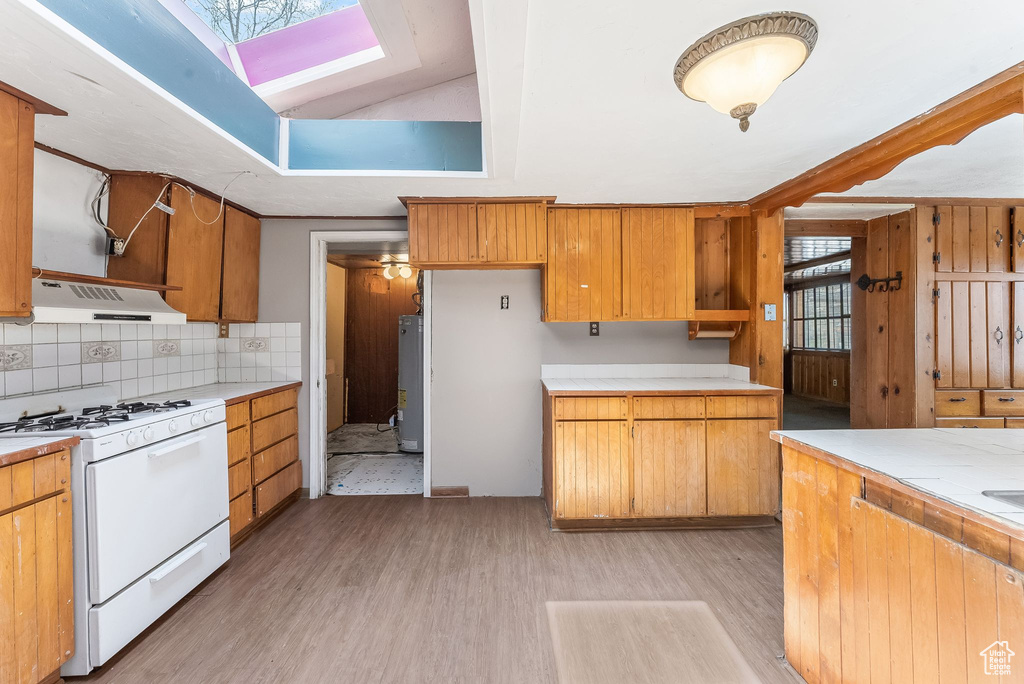 Kitchen with light hardwood / wood-style flooring, tasteful backsplash, white gas range, water heater, and vaulted ceiling with skylight