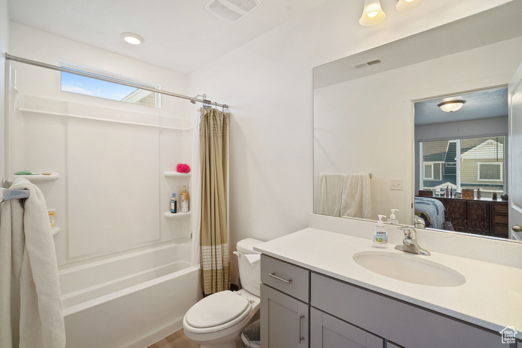Full bathroom with a healthy amount of sunlight, toilet, large vanity, and shower / bathtub combination with curtain
