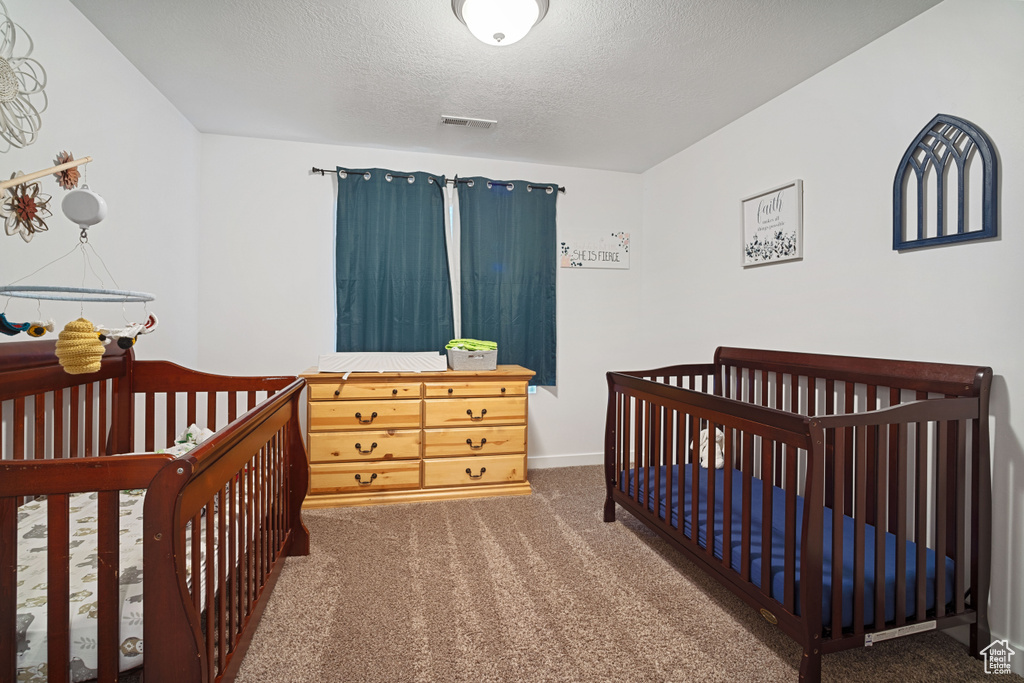 Bedroom with dark colored carpet, a crib, and a textured ceiling