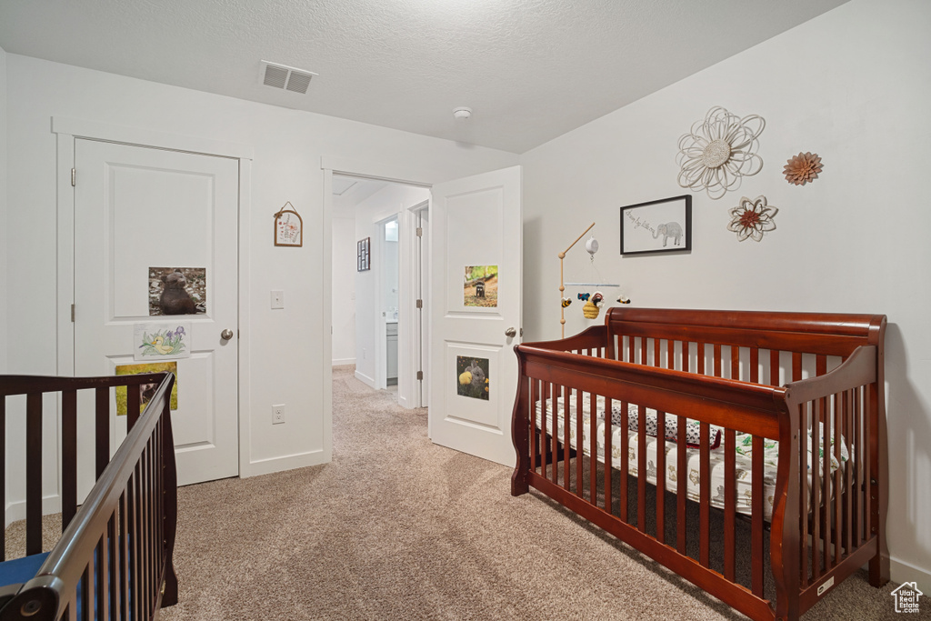 Bedroom featuring light colored carpet, a nursery area, and a textured ceiling
