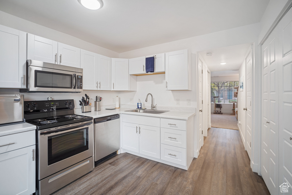Kitchen with white cabinets, sink, appliances with stainless steel finishes, and hardwood / wood-style flooring