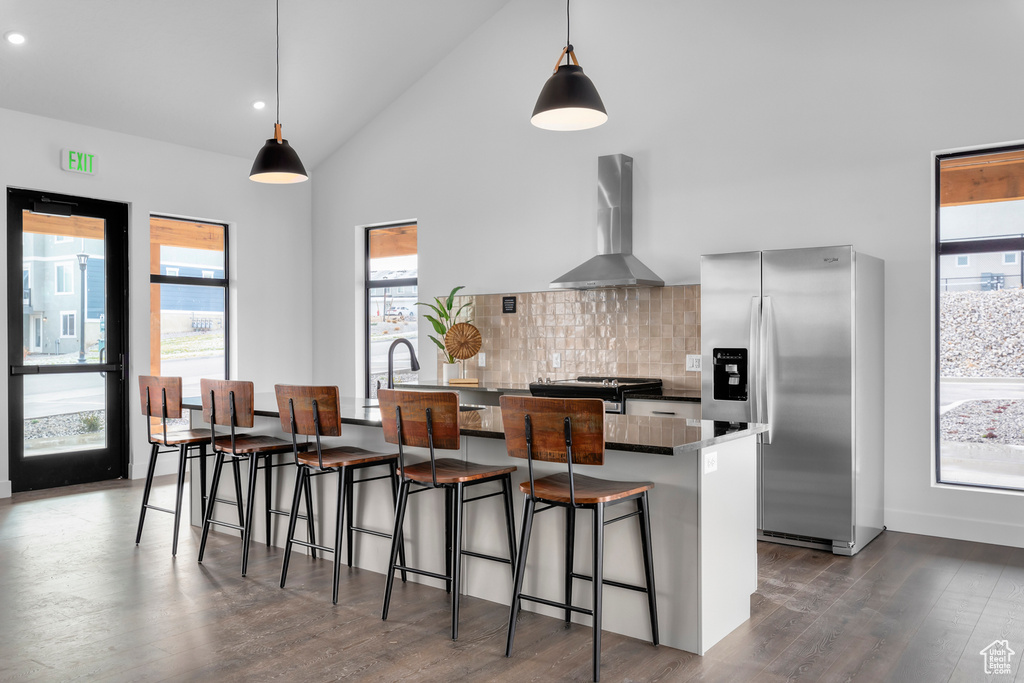 Kitchen featuring plenty of natural light, dark hardwood / wood-style floors, backsplash, wall chimney range hood, and stainless steel fridge with ice dispenser