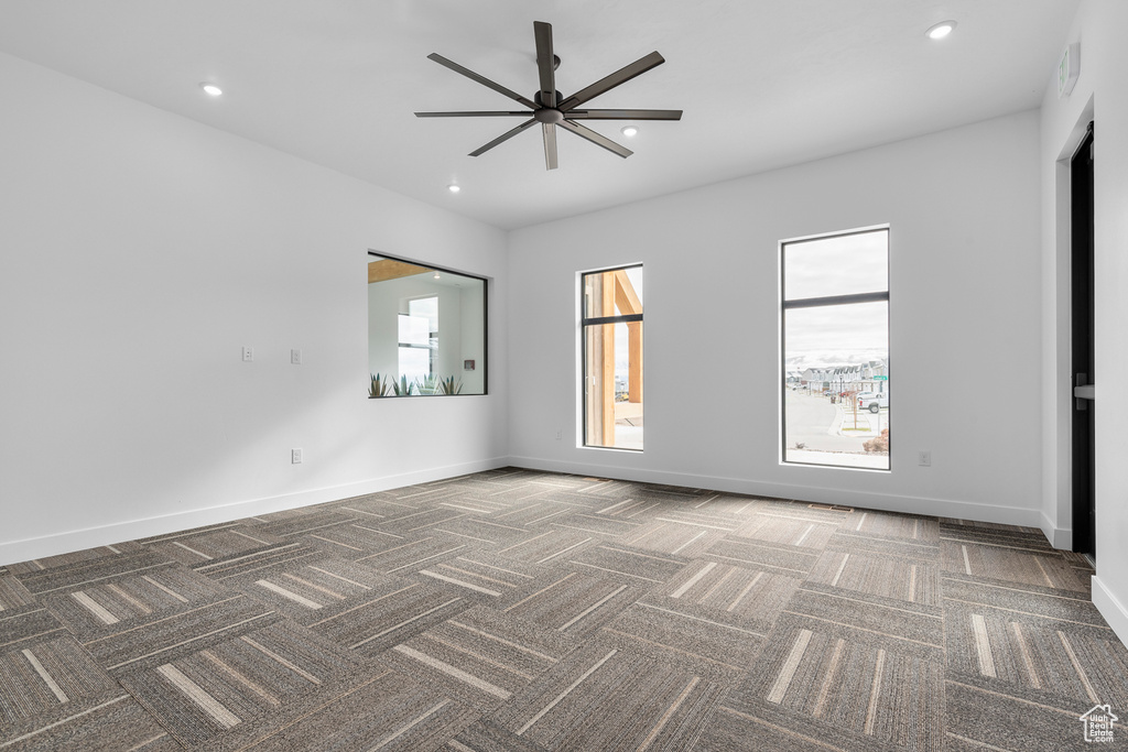 Unfurnished room featuring plenty of natural light, dark colored carpet, and ceiling fan