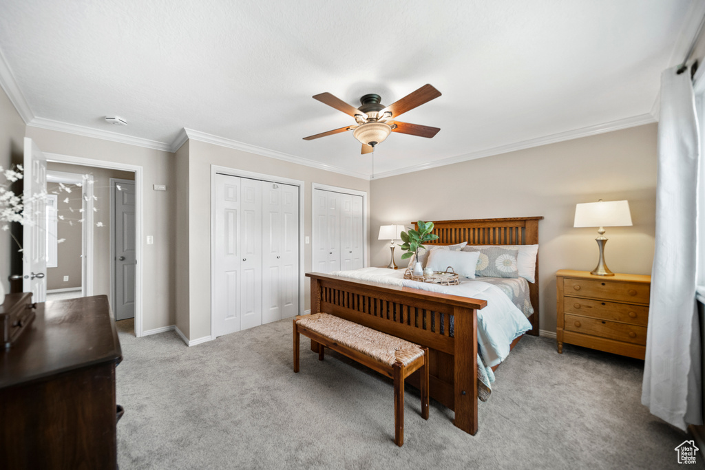 Carpeted bedroom with crown molding, ceiling fan, and multiple closets