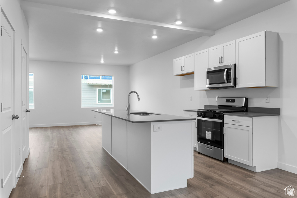 Kitchen with appliances with stainless steel finishes, white cabinets, sink, hardwood / wood-style flooring, and a kitchen island with sink