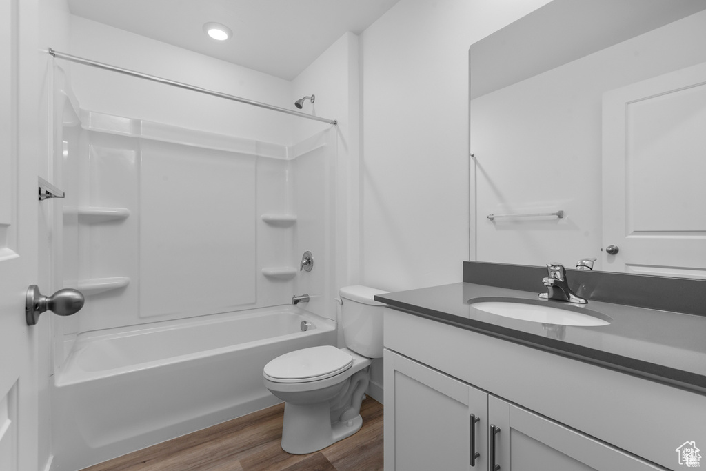 Full bathroom with hardwood / wood-style floors, shower / bathing tub combination, vanity with extensive cabinet space, and toilet