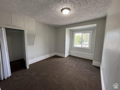 Empty room with a textured ceiling and dark colored carpet