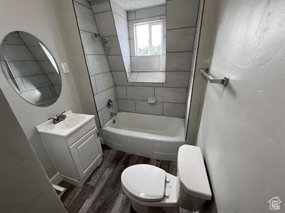 Full bathroom with wood-type flooring, vanity, tiled shower / bath combo, and toilet