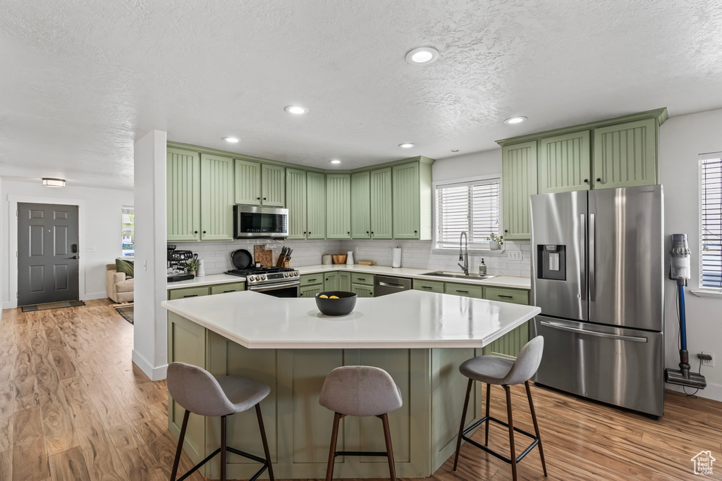 Kitchen with appliances with stainless steel finishes, a kitchen breakfast bar, backsplash, and light hardwood / wood-style flooring